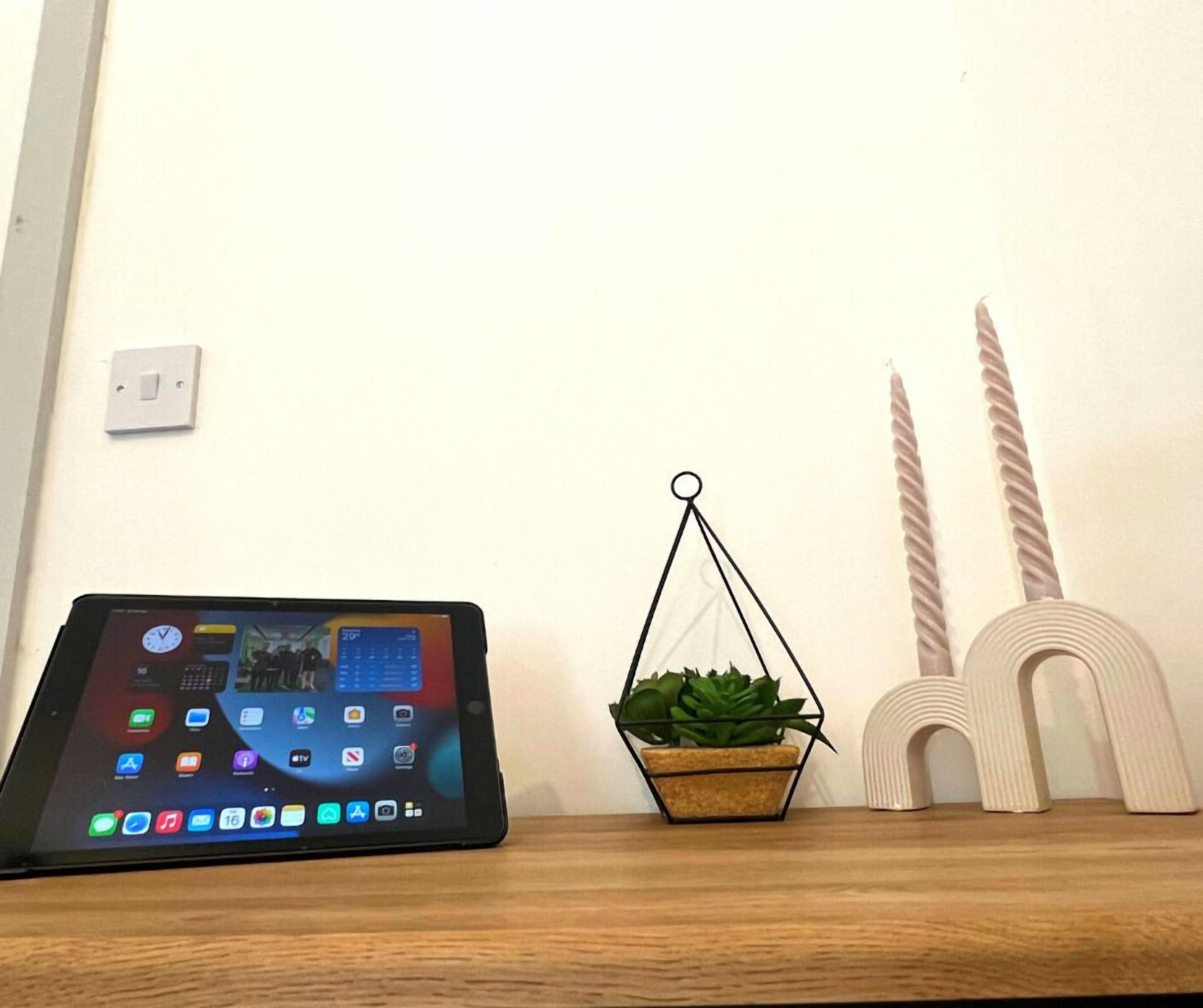 A tablet on a wooden surface, a hanging plant, and two candle holders.