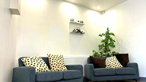 Two grey sofas with polka dot cushions, a small plant, and a shelf with a 'home' sign. - Darlington Suites by SA Stays (Wigan)