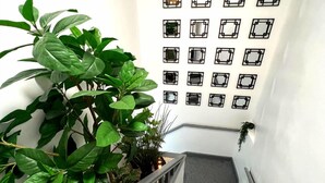 A staircase with a handrail, a potted plant on the left, and a wall with multiple square mirrors. - Darlington Suites by SA Stays (Wigan)