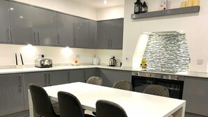 A modern kitchen with grey cabinets, a white countertop, and a built-in oven. There is a dining table with four chairs. - Darlington Suites by SA Stays (Wigan)
