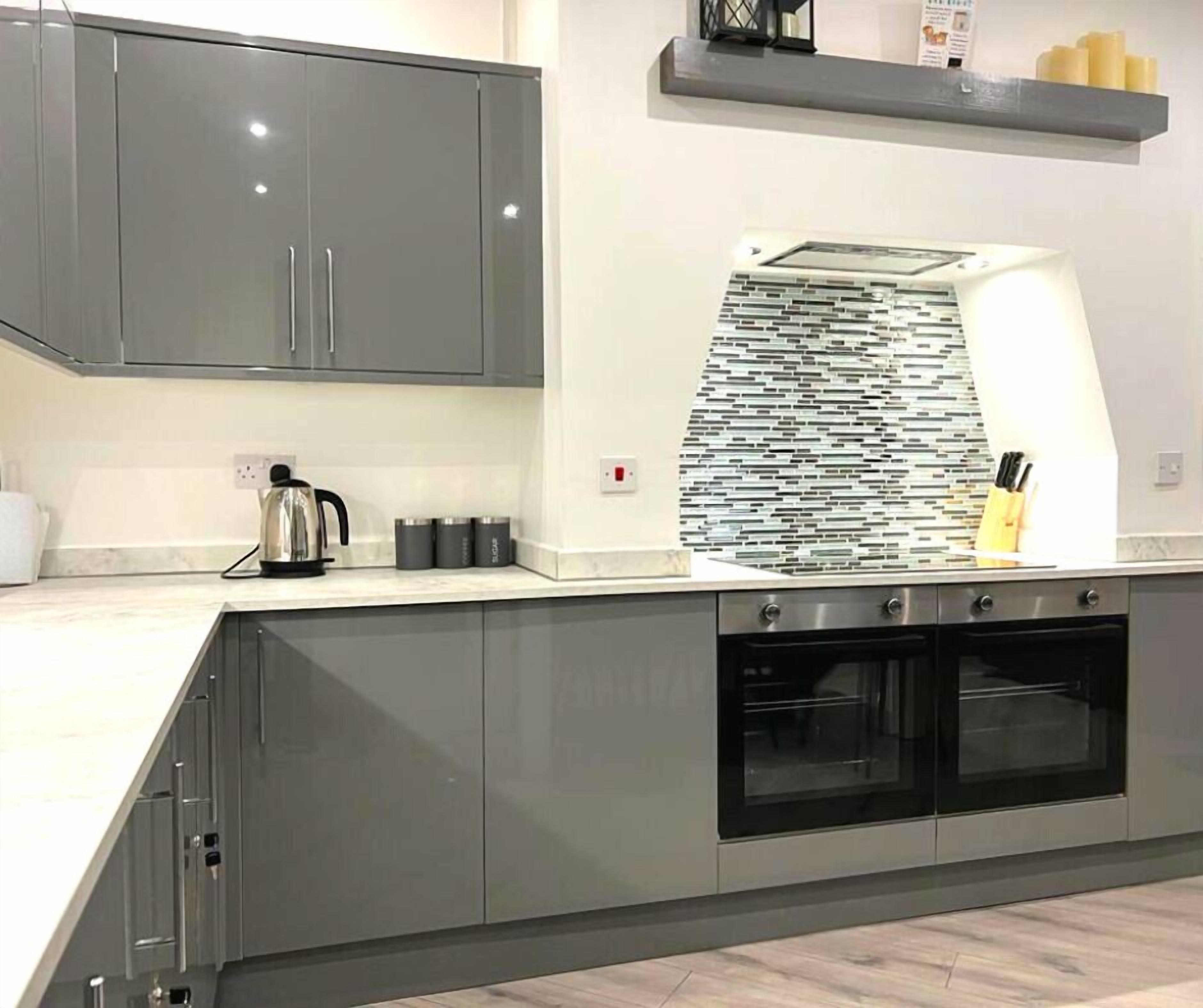 A modern kitchen with grey cabinets, a stainless steel kettle, and a tiled backsplash.