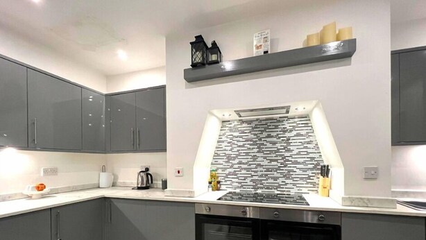 A modern kitchen with grey cabinets, a black and white backsplash, and a stainless steel range hood. - Darlington Suites by SA Stays (Wigan)