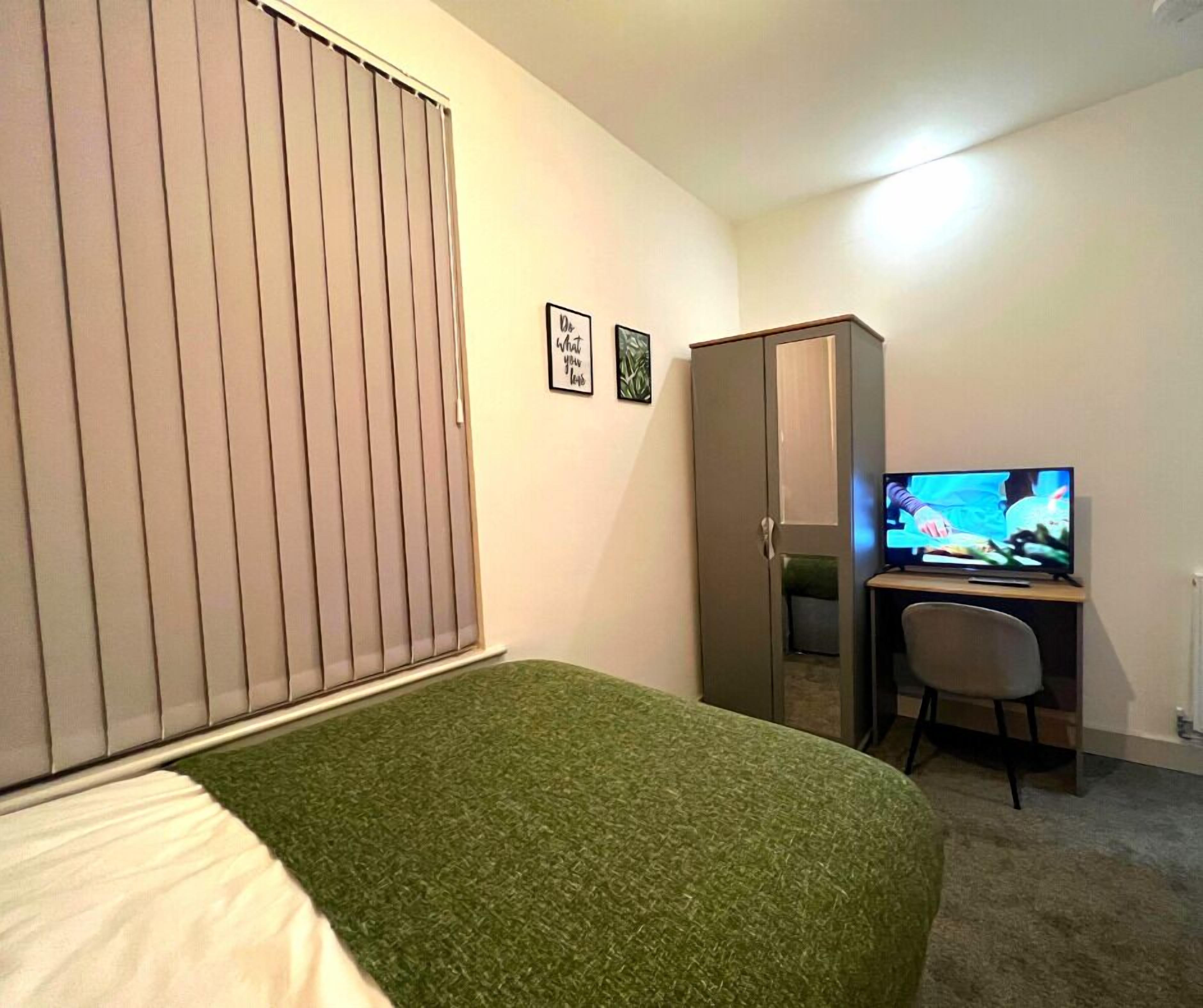 Een slaapkamer met een bed, een bureau met een televisie, een kledingkast en twee foto's in lijsten aan de muur.