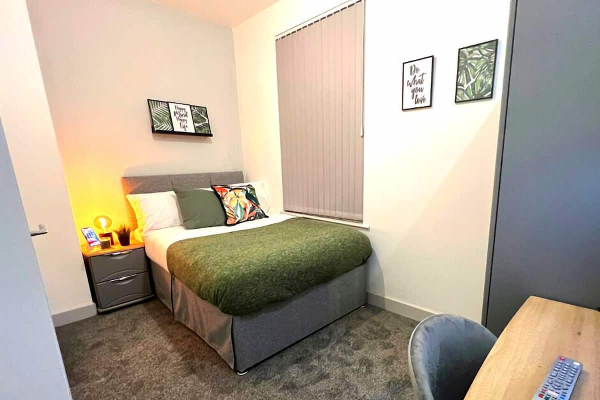 A bedroom with a bed, bedside table, lamp, and a chair.