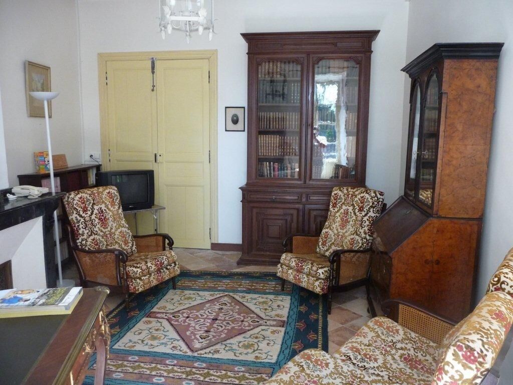 A living room with two patterned armchairs, a wooden cabinet, a television, and a patterned rug.