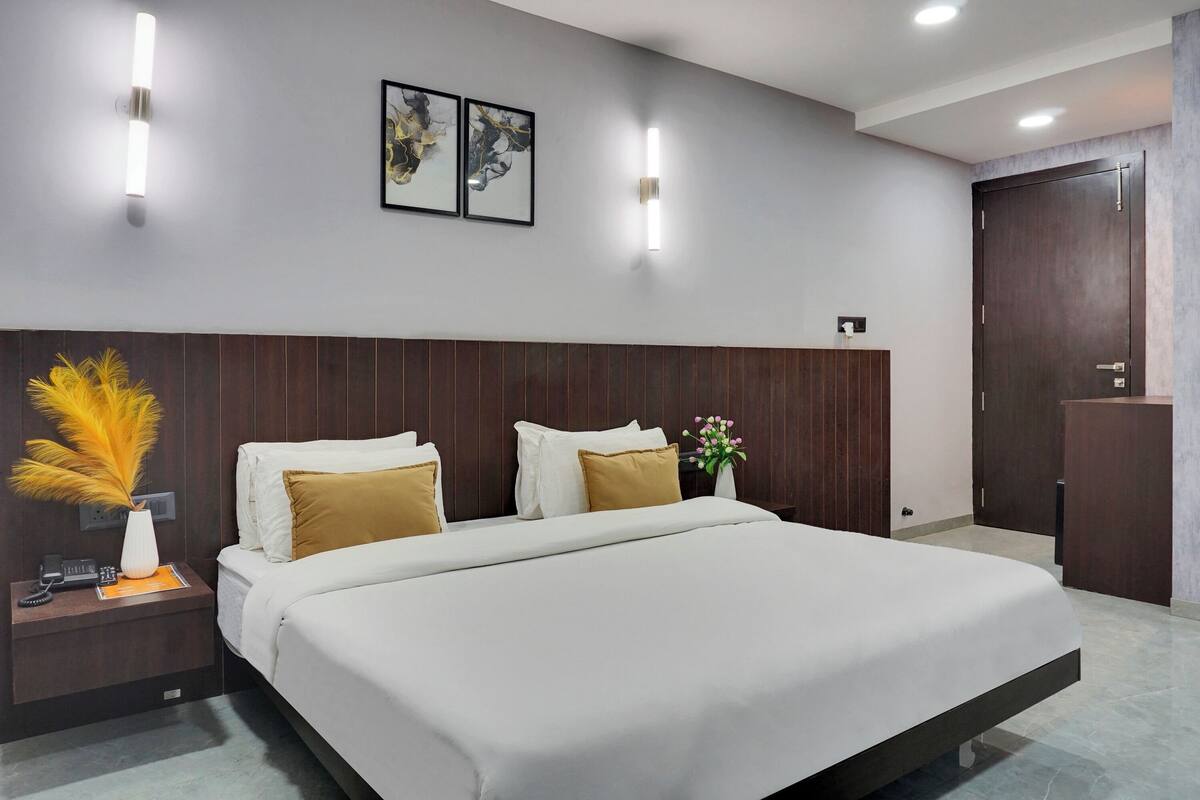 A modern hotel room with a large bed, wooden headboard, and two wall-mounted light fixtures.