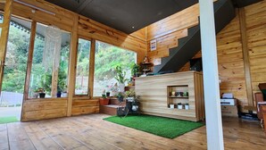 A wooden interior with large windows, a green artificial grass area, and a staircase. - The Mystic Pines (Nainital)