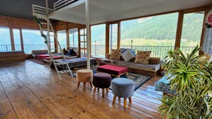 A cozy room with wooden floors, a loft bed, a sofa with cushions, and a large window offering a mountain view. - The Mystic Pines (Nainital)