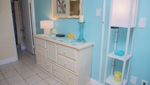 Un baño con tocador blanco, un espejo con marco decorativo, pared azul y repisa blanca con un cubo amarillo.