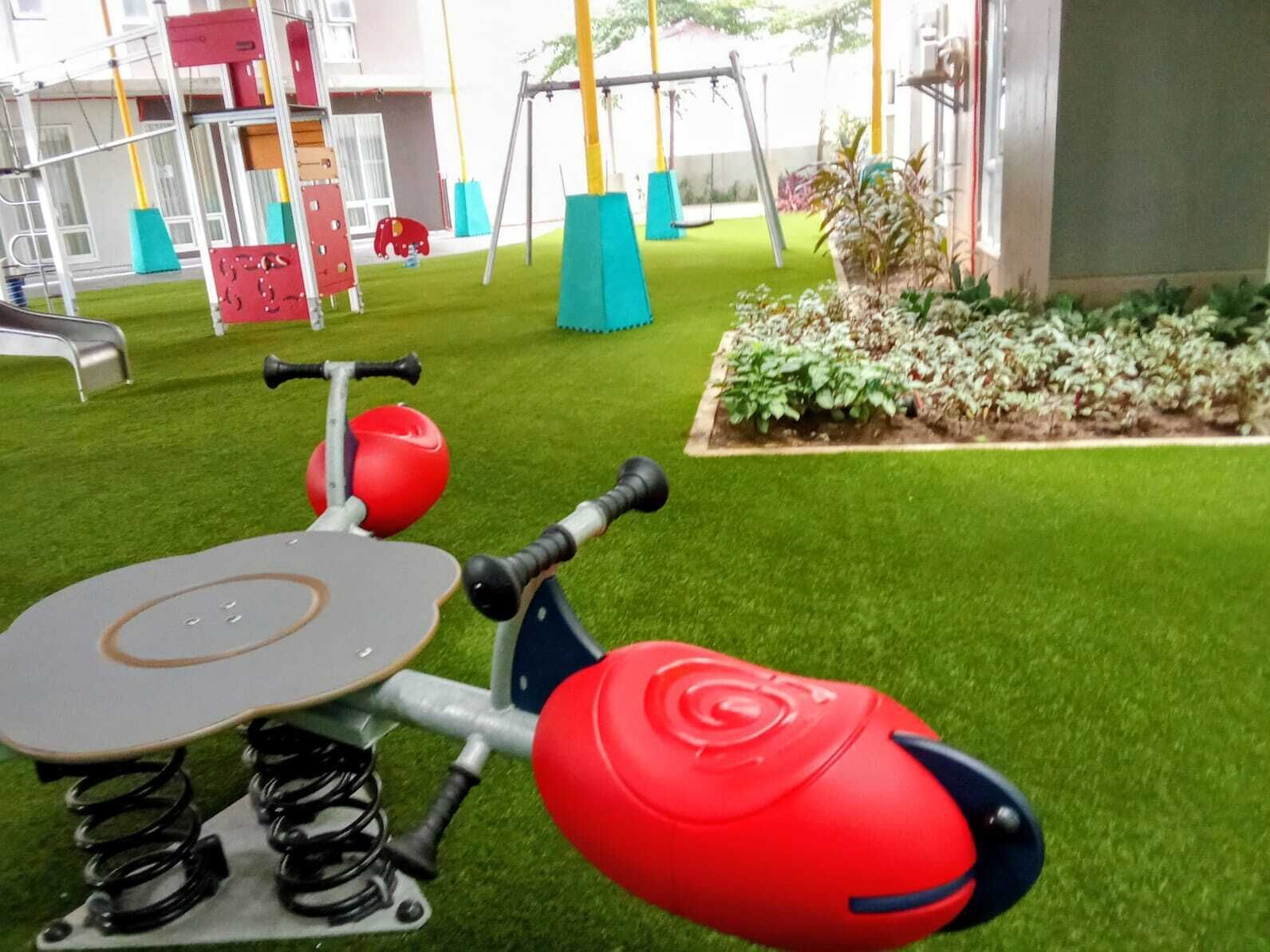 Un espace de jeux pour enfants comprenant un petit vélo d’exercice, une balançoire et un parterre de fleurs.