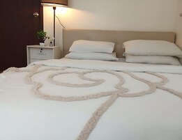 Ein ordentlich bezogenes Bett mit einer weichen, weißen Decke, einer Nachttischlampe und einem kleinen Nachttisch mit einer Pflanze.