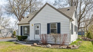 A single-story house with a gabled roof, a front porch, and a small front yard with rocks and shrubs.