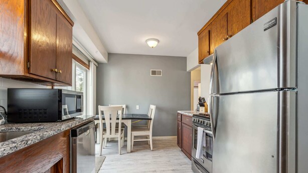A modern kitchen with wooden cabinets, stainless steel appliances, a granite countertop, and a dining area with a table and chairs.