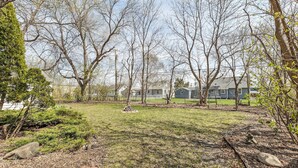 A residential backyard with a lawn, trees, and a stone pathway.