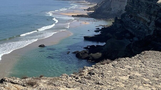 A coastal landscape with a rocky shoreline, a sandy beach, and a cliff overlooking the ocean.