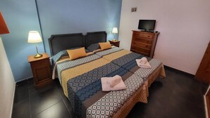 Ein Hotelzimmer mit einem Bett, zwei Nachttischen mit Lampen, einem Fernseher auf einer Holzkommode und einer kleinen Wanddekoration.
