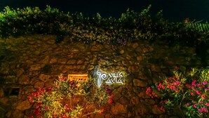 Kivimuuri, jossa on kyltti, jossa lukee ”Villa Amia”, ja kyltti on valaistu lämpimällä valolla.