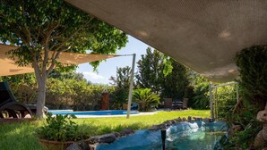 En have med swimmingpool, pergola og et lille vandfald.