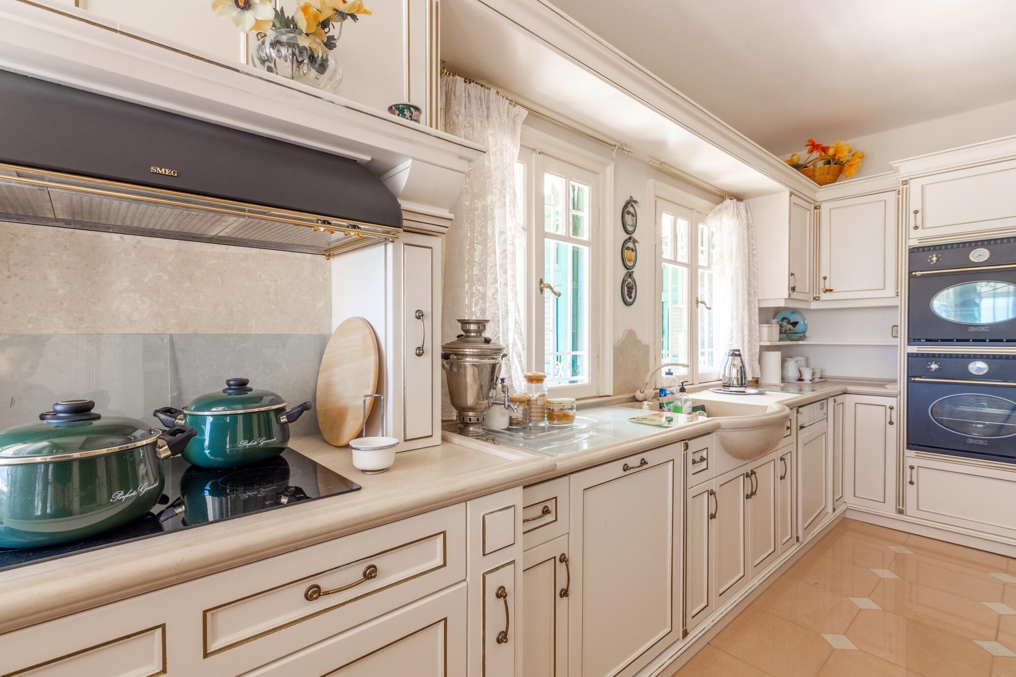 A spacious kitchen with white cabinetry, a black range hood, and a double sink.