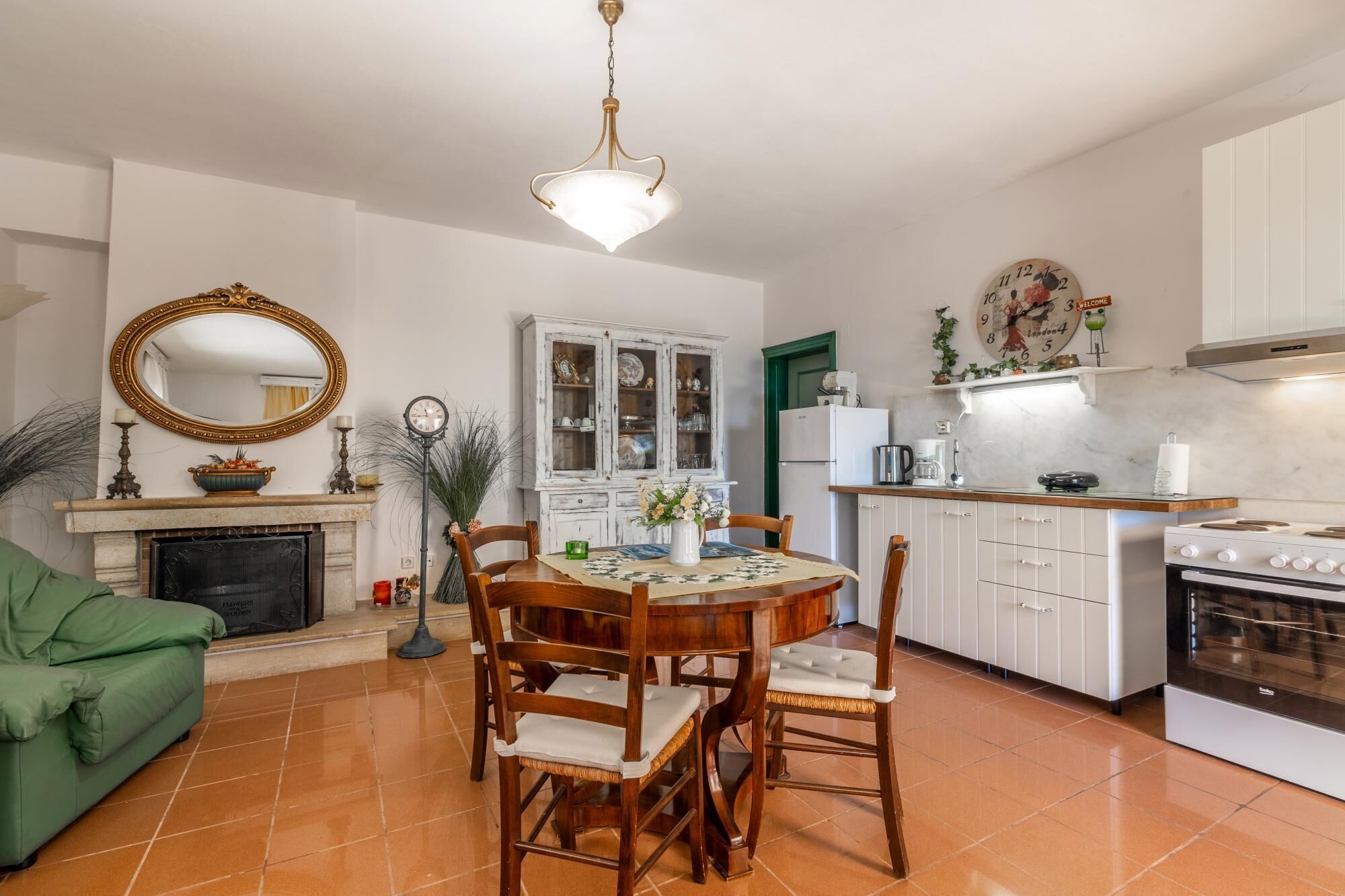 A cozy living room with a fireplace, a dining table with chairs, a green sofa, and a kitchen area with cabinets and appliances.