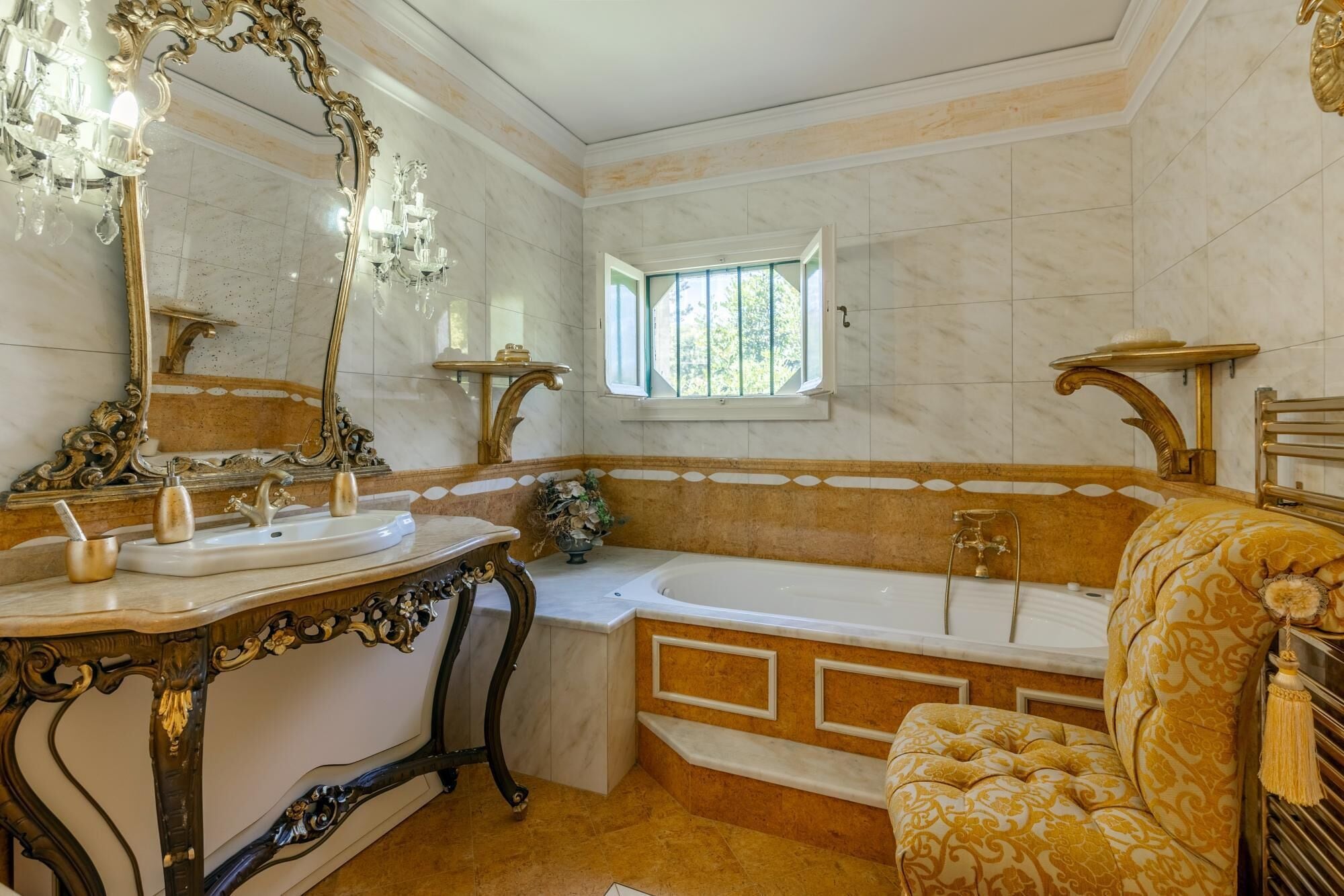 Een luxe badkamer met een grote spiegel, gedetailleerde gouden elementen, een badkuip en een raam dat voor natuurlijk licht zorgt.