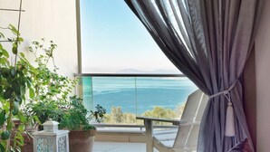 A bedroom with a large bed, a view of the sea, and potted plants on the balcony.