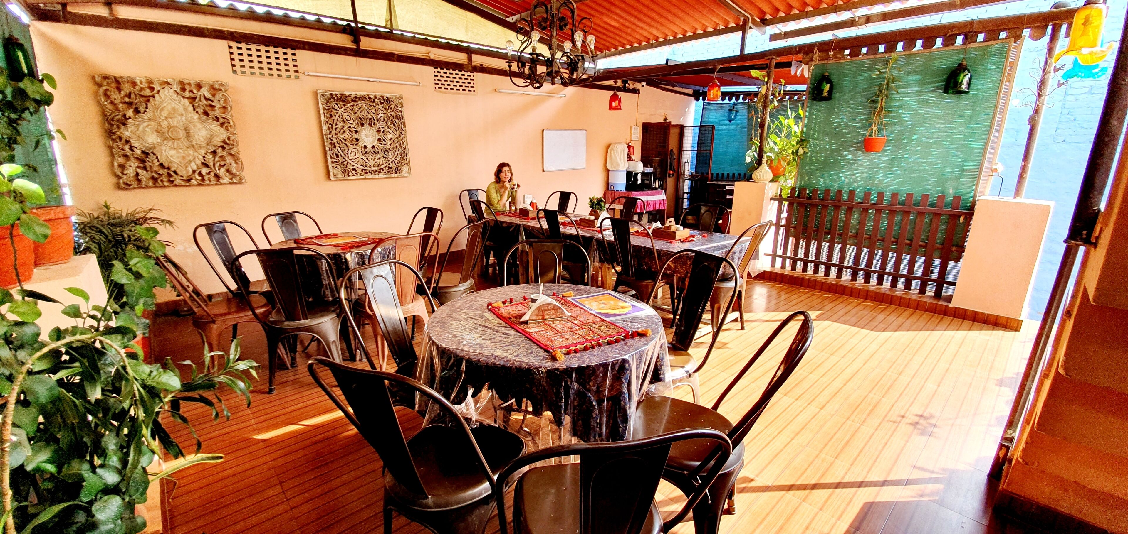An outdoor dining area with multiple tables and chairs, surrounded by potted plants and decorative wall art.