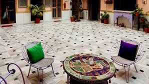 A courtyard with a tiled floor, two-tiered building with balconies, and outdoor seating with cushions. - Durag Niwas (Jodhpur)