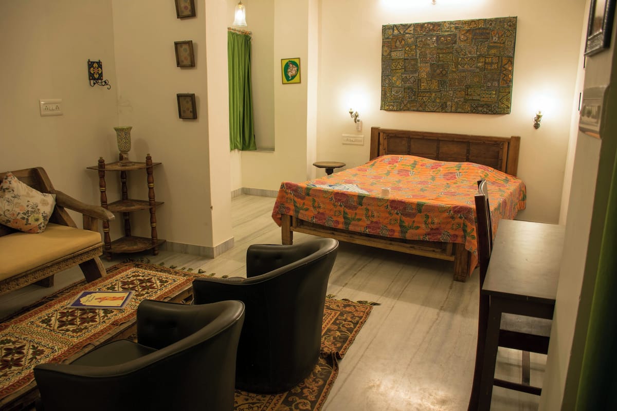 A bedroom with a bed, a chair, a small table, and a sofa.
