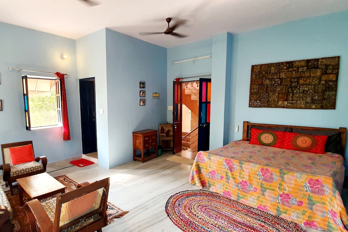 A room with a bed, a desk, chairs, a ceiling fan, and a wall with pictures.