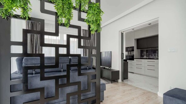 Een moderne woonkamer met een geometrisch wandpaneel, een grijze bank en een televisie.