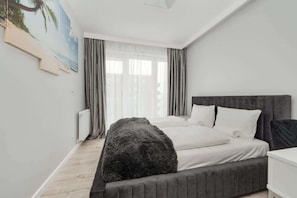 Une chambre à coucher avec un lit, une grande fenêtre avec des rideaux, un radiateur et un tableau accroché au mur.