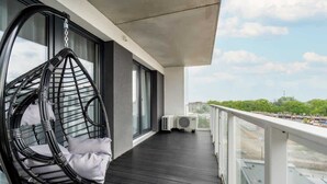 Een balkon met een hangstoel, airconditionings en uitzicht op de stad.