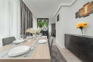 Une salle à manger moderne avec une table en bois dressée pour quatre personnes, une console noire à la texture intéressante et un élément décoratif mural.
