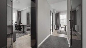 Een moderne hotelkamer met een glazen scheidingswand, een bureau met stoel, een bank en een zithoek met een tafel en stoelen.
