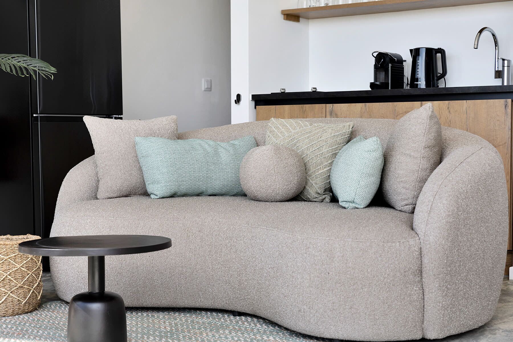 Un salon moderne avec un canapé beige, une table basse ronde noire et un petit panier en osier.