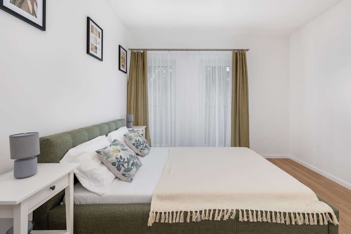 Une chambre à coucher avec un lit, une table de chevet avec une lampe, une fenêtre avec des rideaux et un tableau encadré au mur.