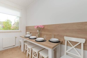 A dining area with a wooden table set for four, white chairs, and a vase with pink flowers. - Spacious Apartment with Balcony | 2 Bedrooms | Gdansk Wrzeszcz (Gdańsk)