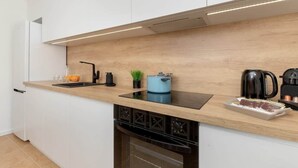 A modern kitchen with white cabinets, a wooden countertop, a built-in dishwasher, a sink, a kettle, and a coffee maker. - Spacious Apartment with Balcony | 2 Bedrooms | Gdansk Wrzeszcz (Gdańsk)