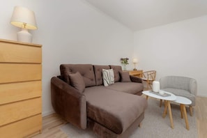 A modern living room with a brown sofa, a small round table, and a wooden cabinet. - Spacious Apartment with Balcony | 2 Bedrooms | Gdansk Wrzeszcz (Gdańsk)