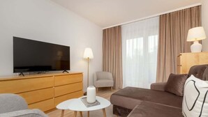 A modern hotel room with a flat-screen TV on a wooden cabinet, a grey sofa, a brown sofa, a small white table, and a lamp. - Spacious Apartment with Balcony | 2 Bedrooms | Gdansk Wrzeszcz (Gdańsk)