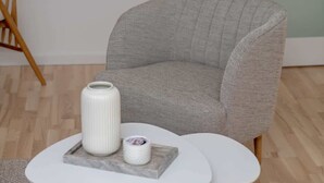 A grey upholstered armchair with a textured fabric, a white round table with a marble base, and a white cylindrical vase on the table. - Spacious Apartment with Balcony | 2 Bedrooms | Gdansk Wrzeszcz (Gdańsk)