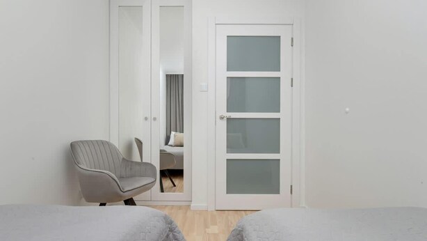 A room with two beds, a chair, and a door leading to another room. - Spacious Apartment with Balcony | 2 Bedrooms | Gdansk Wrzeszcz (Gdańsk)