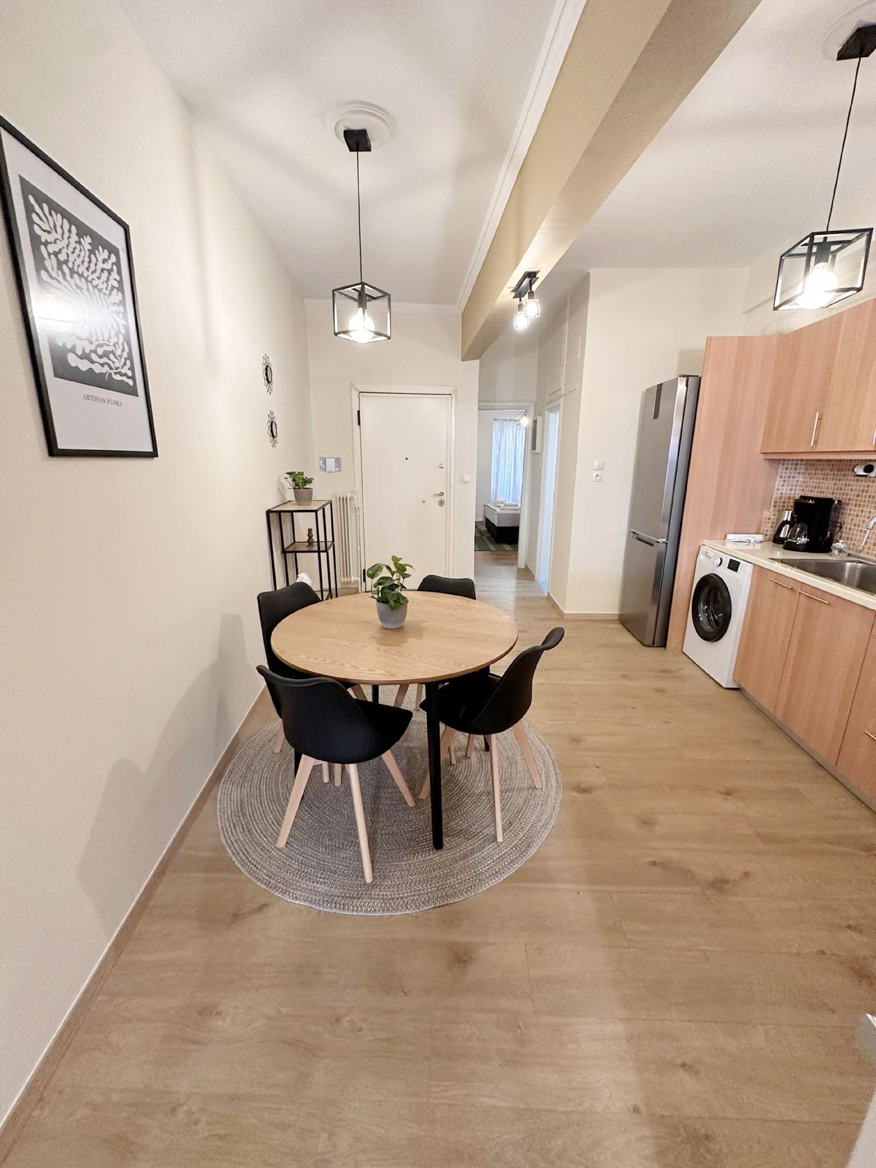 Una cocina moderna con comedor, que presenta una mesa redonda de madera, sillas negras, una lámpara colgante y una lavadora.