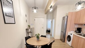 A modern kitchen with a dining area, featuring a round wooden table, black chairs, a hanging light fixture, and a washing machine.