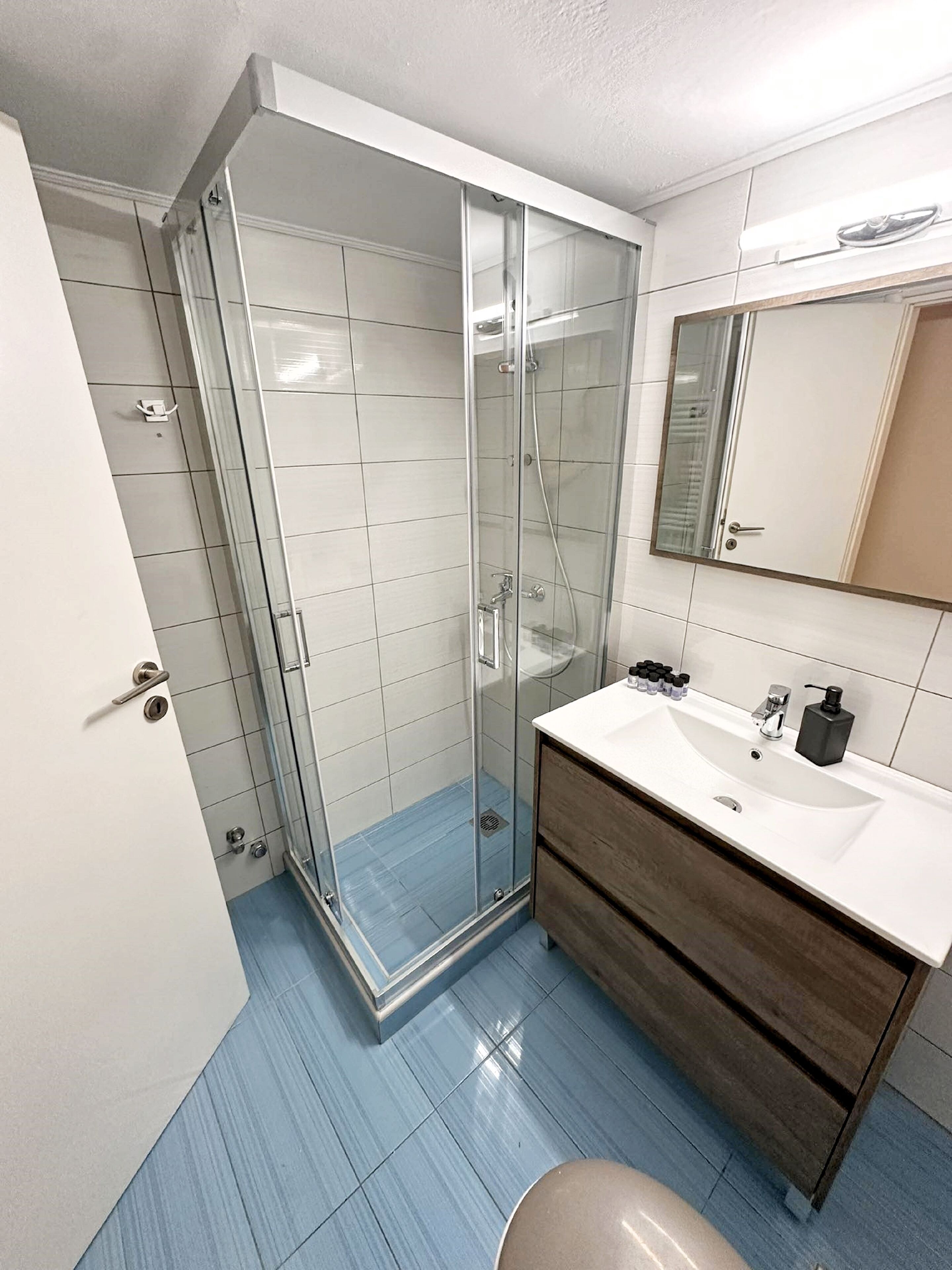 A modern bathroom with a glass shower enclosure, a white sink with a wooden vanity, and a large mirror above the sink.
