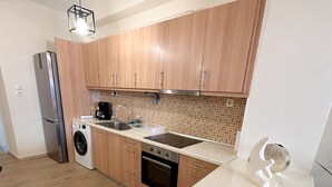 A modern kitchen with wooden cabinets, a stainless steel refrigerator, a washing machine, and a dishwasher.