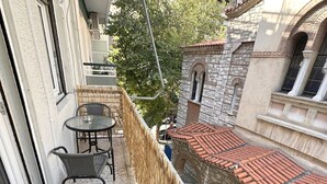 A balcony with a table and chairs, a woven fence, and a view of a stone building with a tiled roof.
