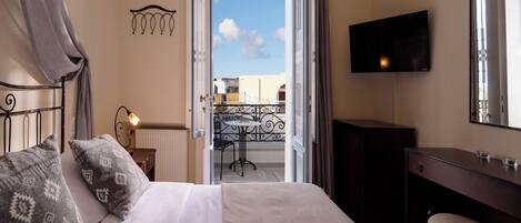 Habitación de hotel con cama, escritorio, televisor y balcón con vistas al cielo.