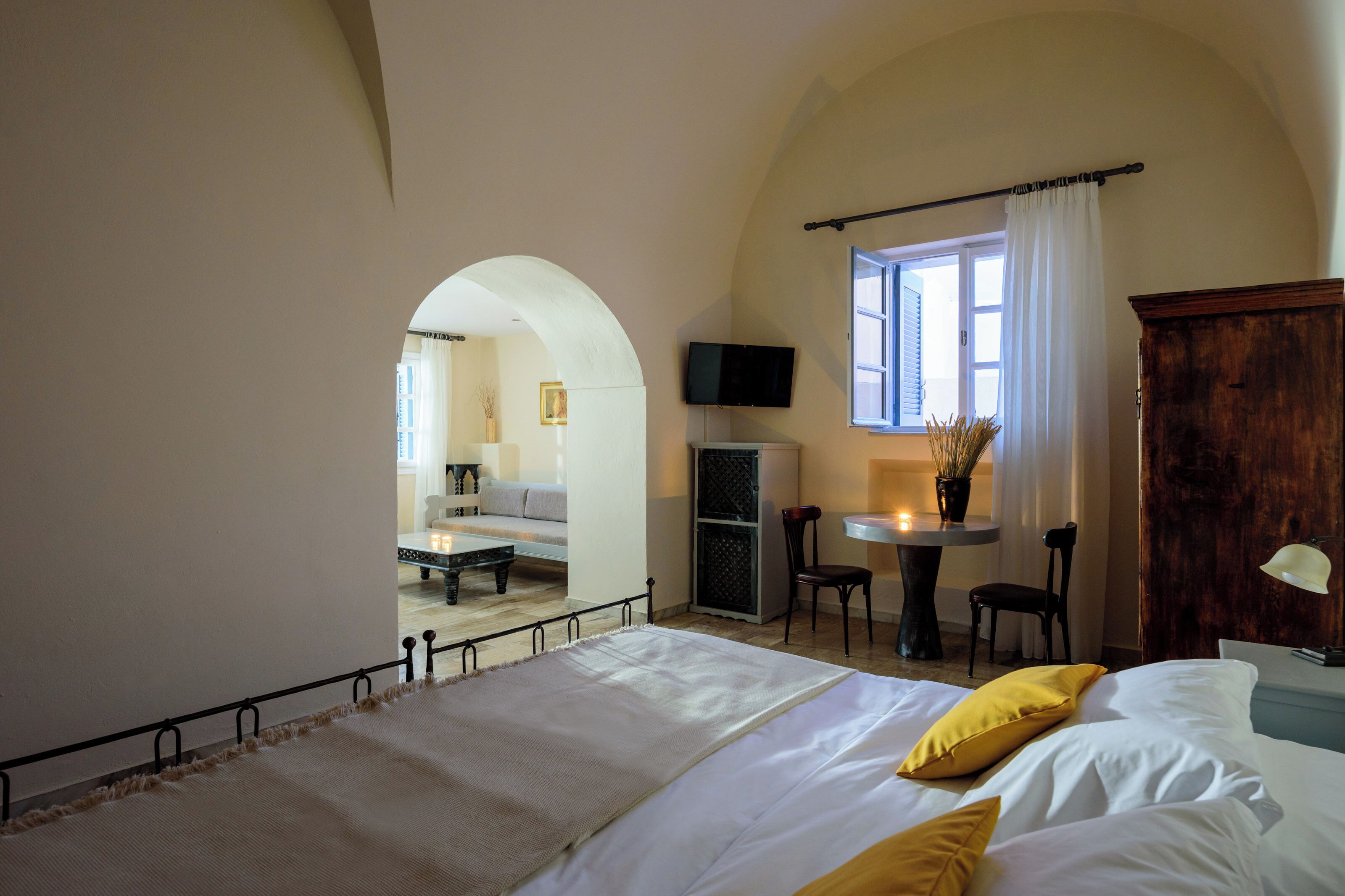Un dormitorio con cama, escritorio, silla, televisor y ventana con cortinas.